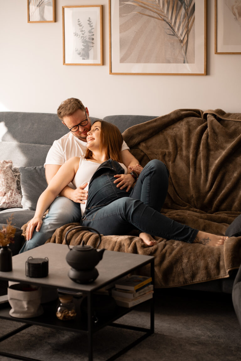 Ein Mann und eine schwangere Frau liegen auf der Couch und freuen sich auf ihr Baby